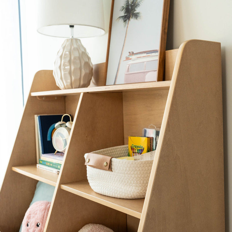 Children's wooden shelf with woven storage basket and Crayola crayons, stacked books, retro alarm clock, beige ceramic lamp and framed palm tree print for nursery organization and decor