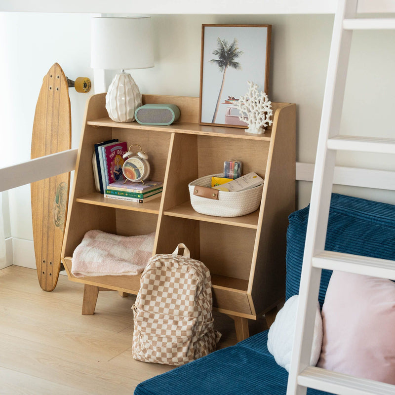 Coastal kids' bedroom wooden cubby organizer with lamp, framed palm print, decorative coral sculpture, longboard skateboard, alarm clock, children's books, woven storage basket and checkered backpack