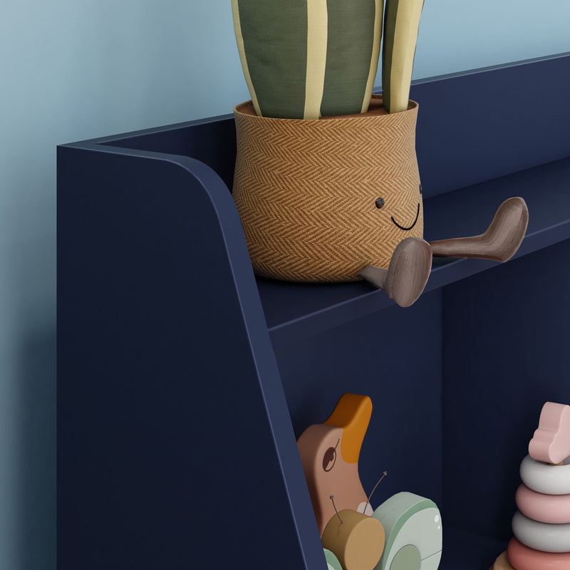 Navy blue shelf in a nursery holding a woven smiley plant pot with green striped fabric leaves, wooden toy banana and snail, and pastel stacking rings — modern kids room decor