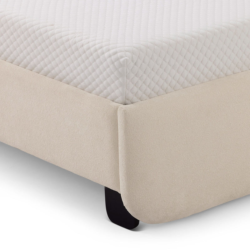 Close-up of quilted white mattress cover on corner of mattress over a beige upholstered bed base with visible black leg