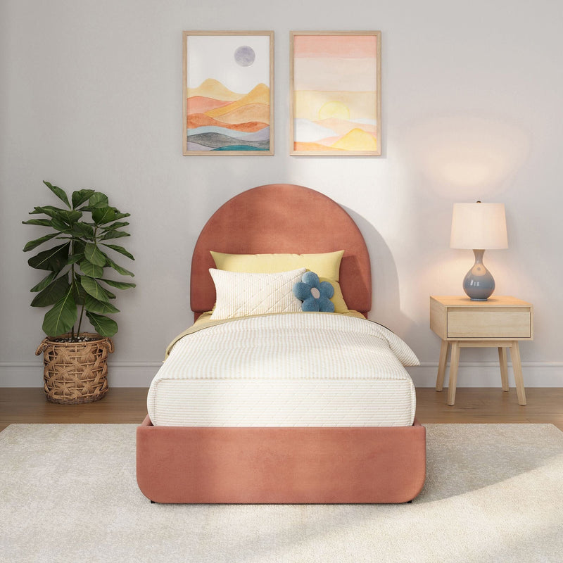 Modern bedroom with coral upholstered round headboard, yellow bedding and blue flower pillow, abstract framed wall art, wicker potted plant and wooden nightstand with lamp