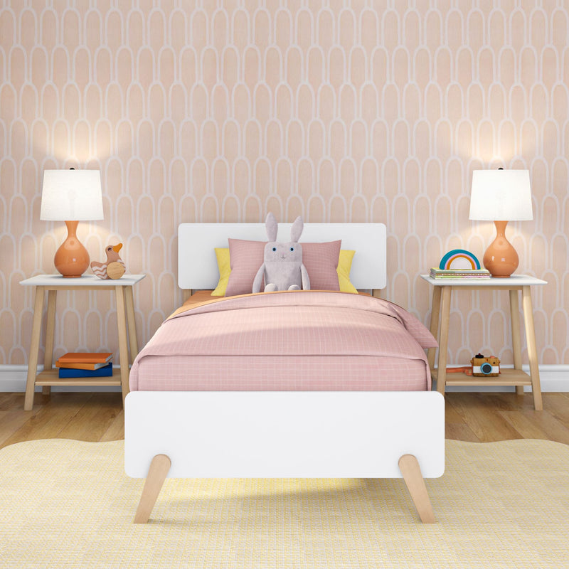 Kids bedroom with pink bedding and plush bunny on a white bed, orange table lamps on wooden nightstands, pastel arch wallpaper and rainbow decor