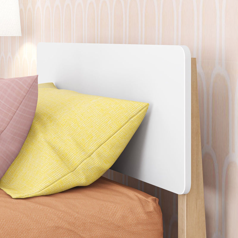 Modern bedroom with white headboard and wooden frame, yellow and blush pillows on textured peach bedding, bedside lamp and patterned wallpaper