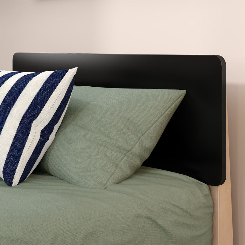Close-up of modern black rounded headboard and wooden bed frame with sage green bedding and navy-and-white striped throw pillow, minimalist bedroom decor