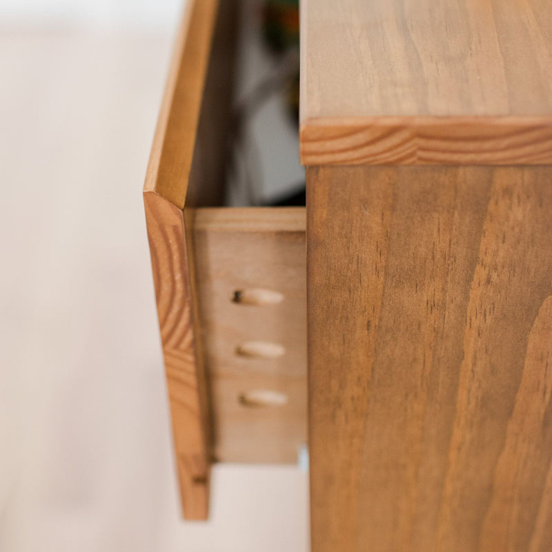Close-up of a partially open wooden dresser drawer showing natural wood grain, warm finish, and furniture detail