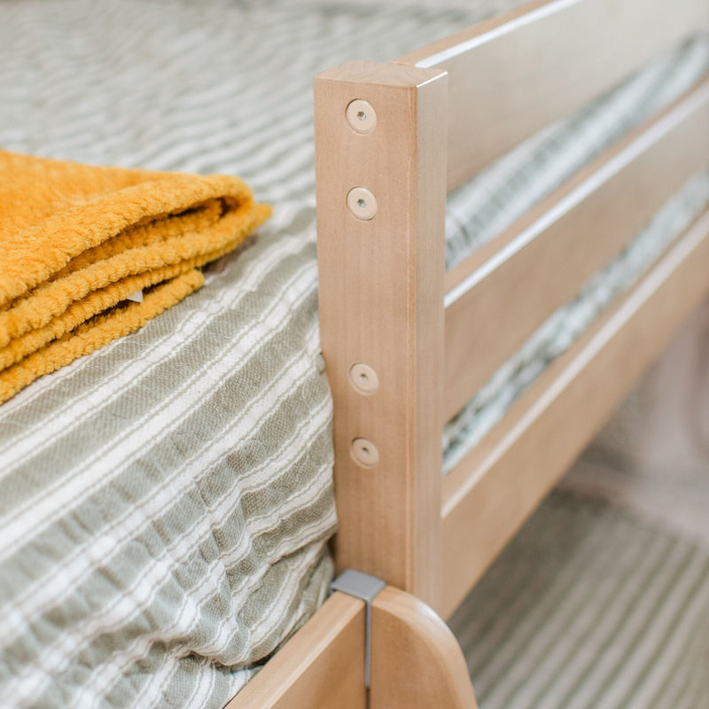 Close-up of natural wooden bed frame and slatted guardrail with striped green bedding and folded yellow fleece blanket in bedroom