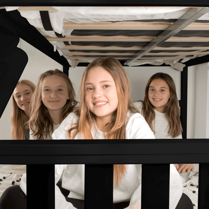 Four smiling teenage girls sitting together on a lower bunk bed in a cozy bedroom — candid sleepover friends portrait