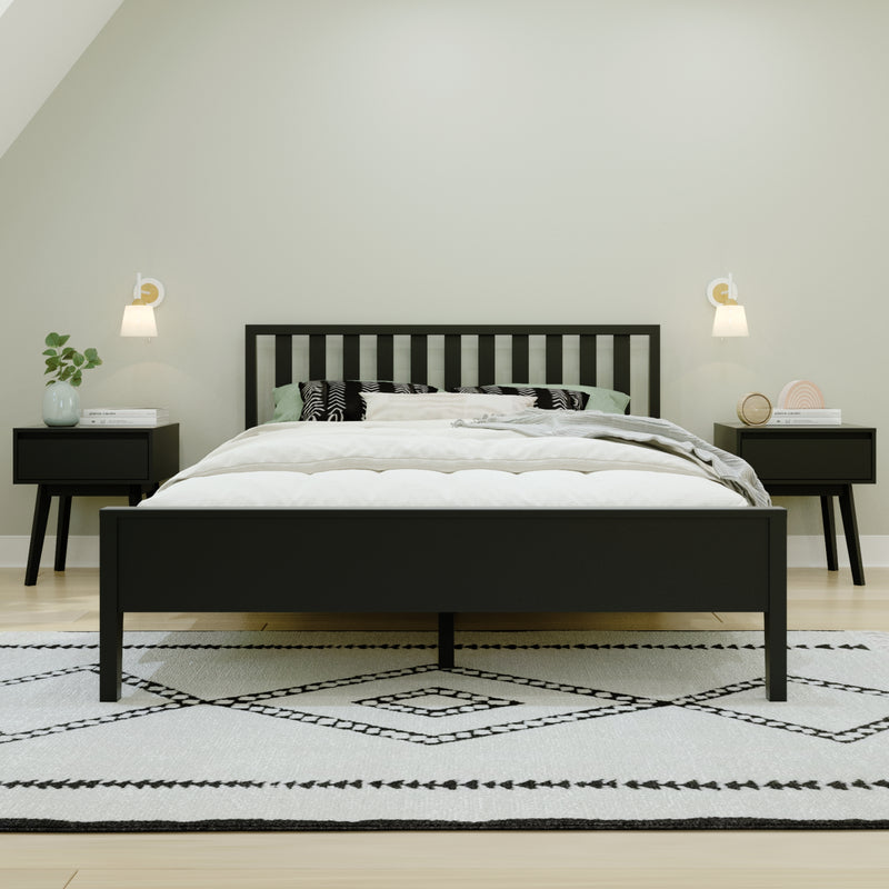 Minimalist modern bedroom with black wooden bed frame, neutral bedding, patterned black-and-white rug, matching nightstands, wall sconces and potted plant