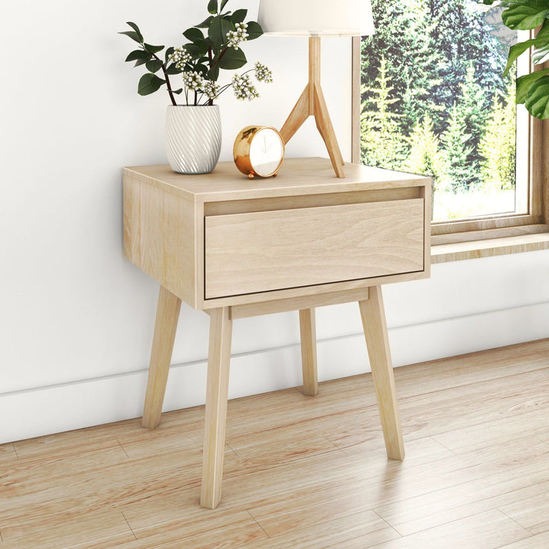 Minimalist Scandinavian light wood bedside table with single drawer and tapered legs, styled with lamp, white vase and gold clock by window