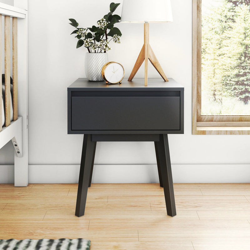 Modern black bedside table with mid-century wooden legs, lamp, potted plant and gold alarm clock in bright minimalist Scandinavian bedroom