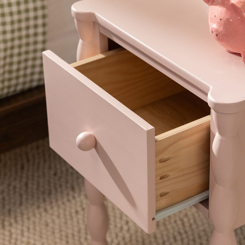 Pink bedside table with open drawer showing natural wood interior, turned legs and ceramic piggy bank on top, children's nursery nightstand
