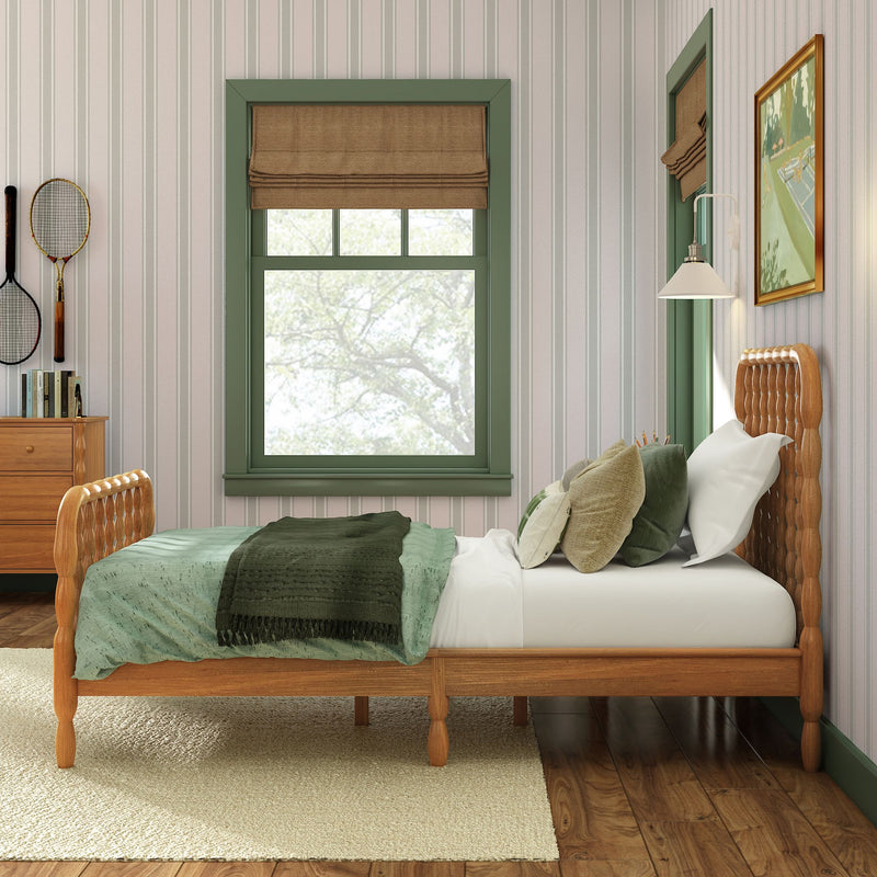 Cozy rustic bedroom interior with carved wooden bed, green bedding and pillows, striped wallpaper, green-trimmed window with brown Roman shade, bedside lamp and dresser with tennis rackets