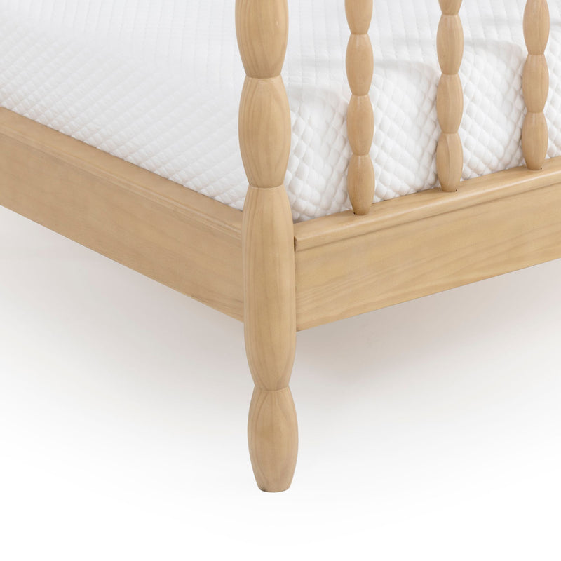 Close-up of light wood spindle bed frame corner with white quilted mattress cover and natural maple finish