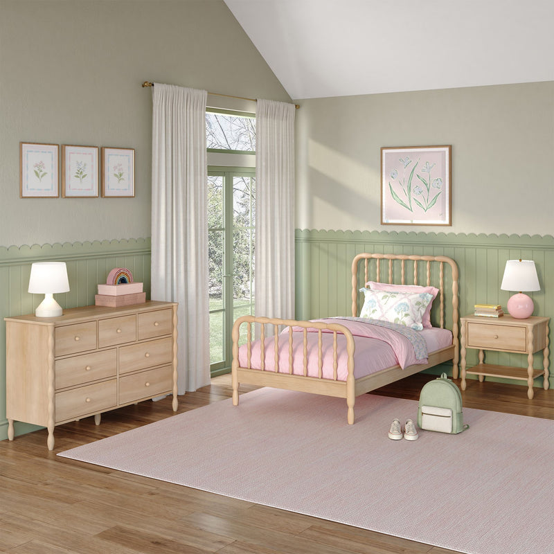Pastel green children's bedroom with wooden spindle bed, pink bedding, light wood dresser and nightstand, scalloped wainscoting, floral wall art, cream curtains and soft natural light.