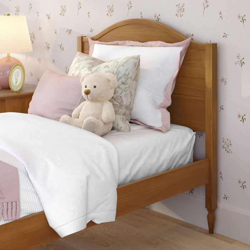 Children's bedroom with wooden headboard, pink bedding and pillows, plush teddy bear, floral wallpaper and bedside lamp.