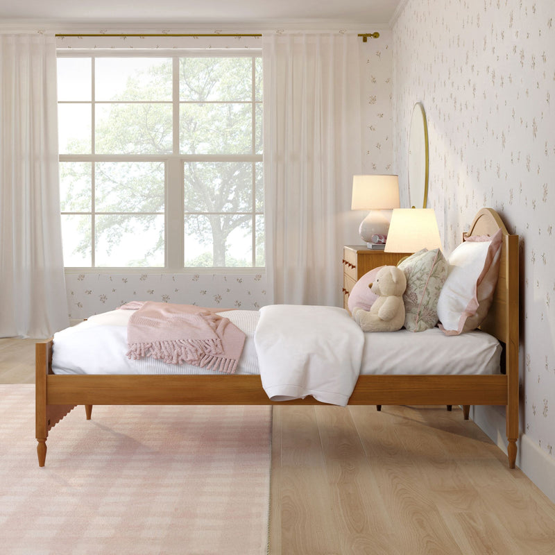 Cozy pastel pink children's bedroom with wooden bed frame, plush teddy bear and pillows, textured throw blanket, bedside lamps, floral wallpaper and large window with sheer curtains bathing the room in soft natural light