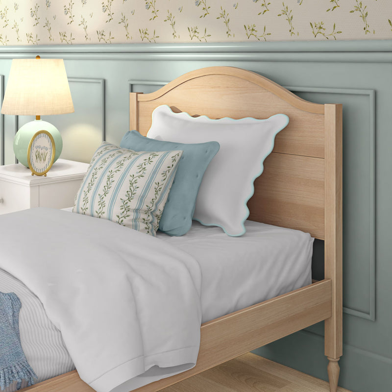 Pastel bedroom decor with wooden headboard, scalloped white and blue pillows, floral striped cushion, mint bedside table with lamp and floral wallpaper