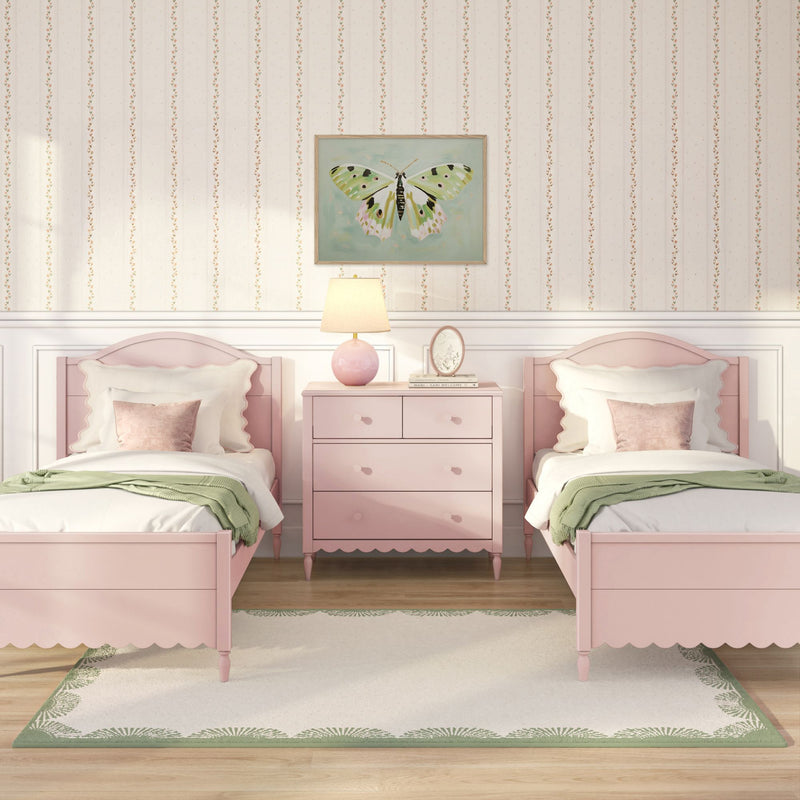 Pink twin girls' bedroom with scalloped headboards, matching pink nightstand and lamp, green throw blanket, butterfly wall art and floral striped wallpaper