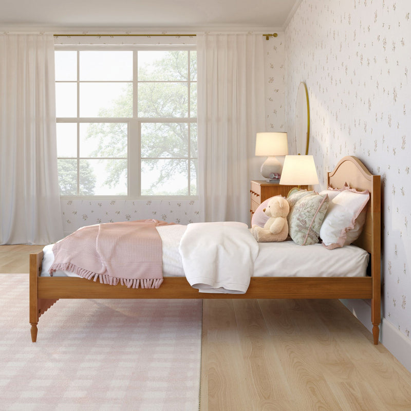 Cozy pastel girls' bedroom nursery with wooden bed frame, pink bedding and throw, floral wallpaper, teddy bear, bedside lamp and large window with sheer curtains