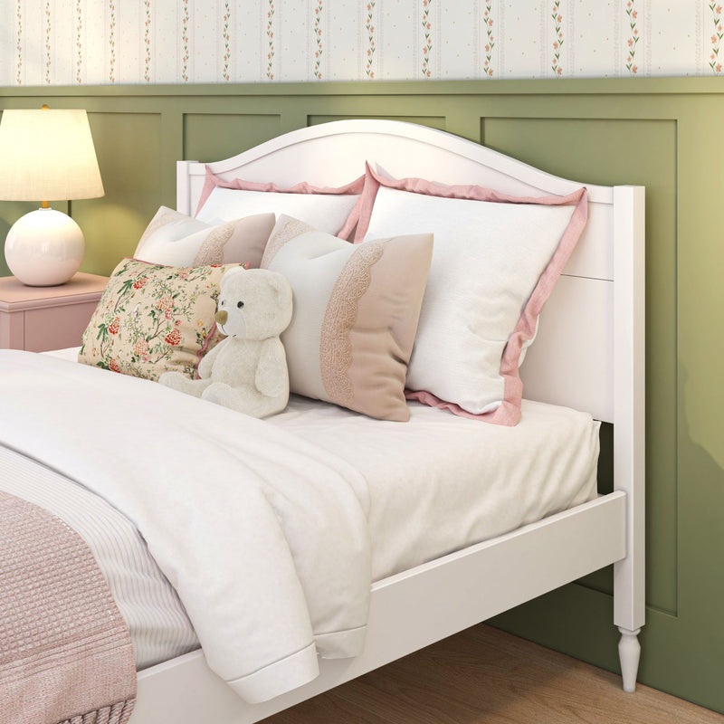 Cozy white bed with pink pillows, floral cushion and teddy bear next to a lamp and green wainscoting in a children's bedroom