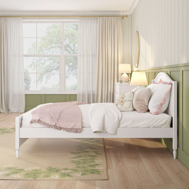 Cozy pastel pink girl's bedroom interior with white bed, plush teddy bear, bedside lamp and round mirror, large window with sheer curtains, green wainscoting and floral rug