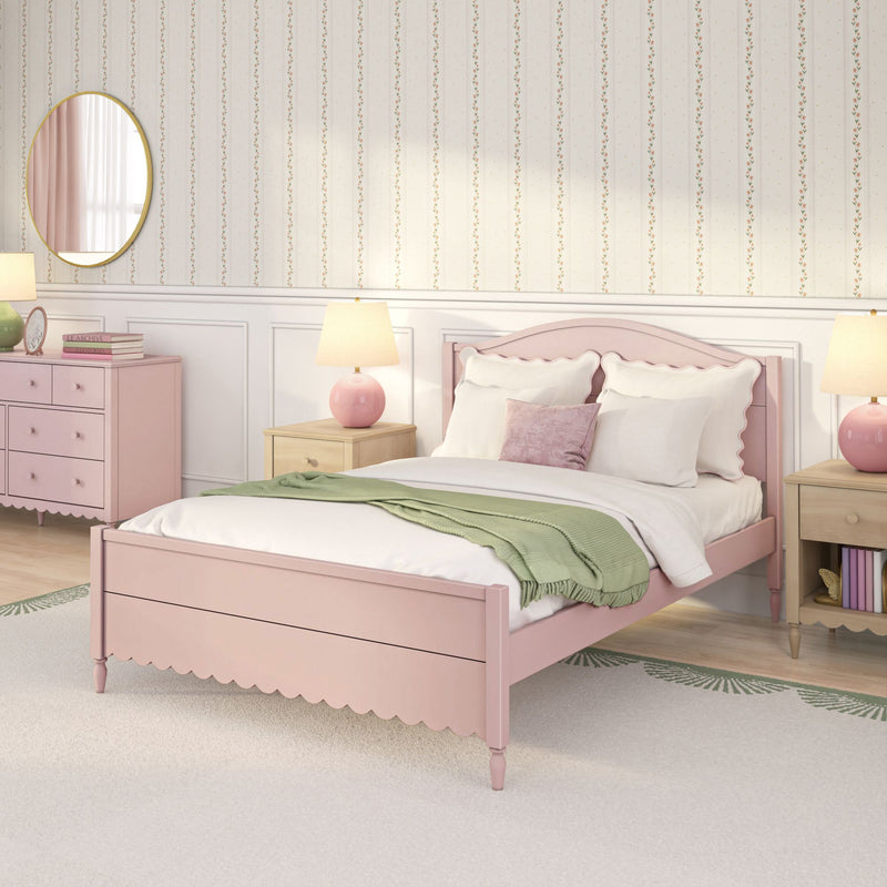 Pastel pink girls' bedroom interior with scalloped headboard bed, white pillows and green throw blanket, wooden nightstand with pink lamp, pink dresser stacked with books and round mirror, and floral striped wallpaper — feminine kids' room decor
