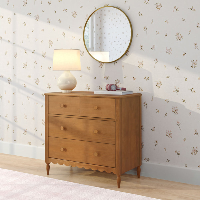 Wooden dresser with round gold mirror, ceramic table lamp and pink headphones against cream floral wallpaper – cozy bedroom decor