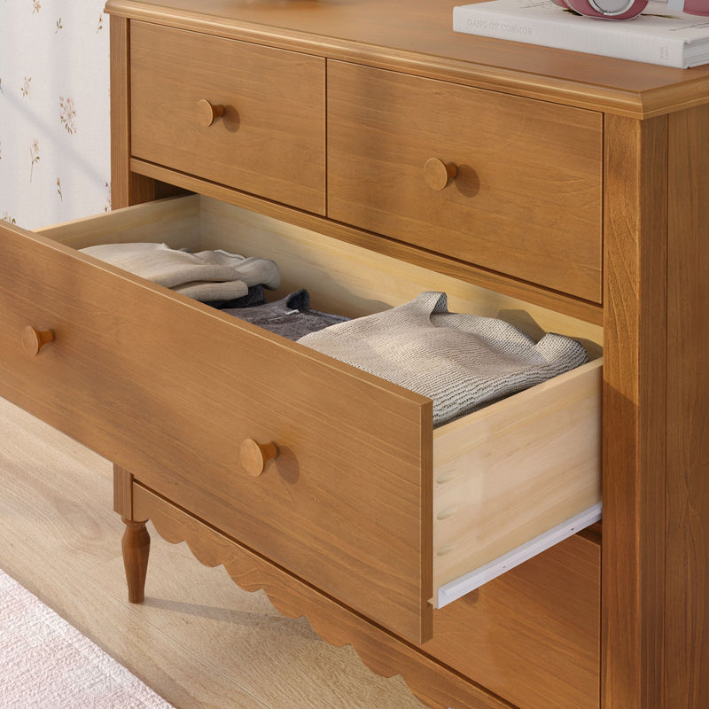 Solid wood dresser with round wooden knobs and open drawer revealing folded sweaters, natural wood finish bedroom storage