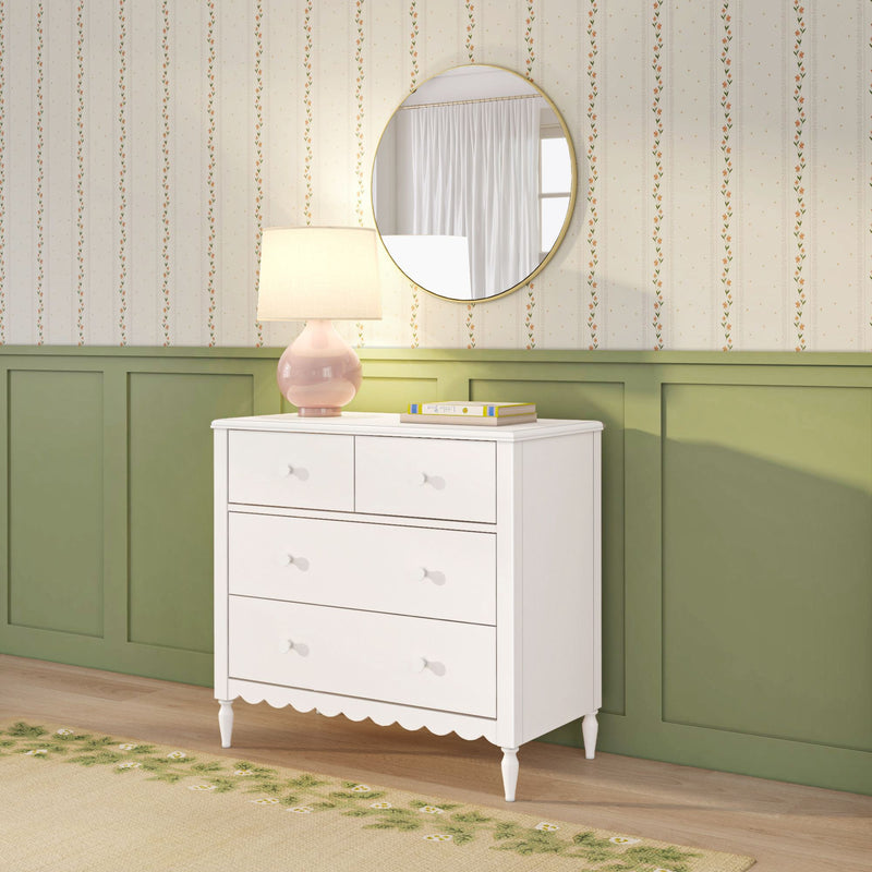 White dresser with pink ceramic lamp and round gold mirror over green wainscoting and cream floral wallpaper in bedroom