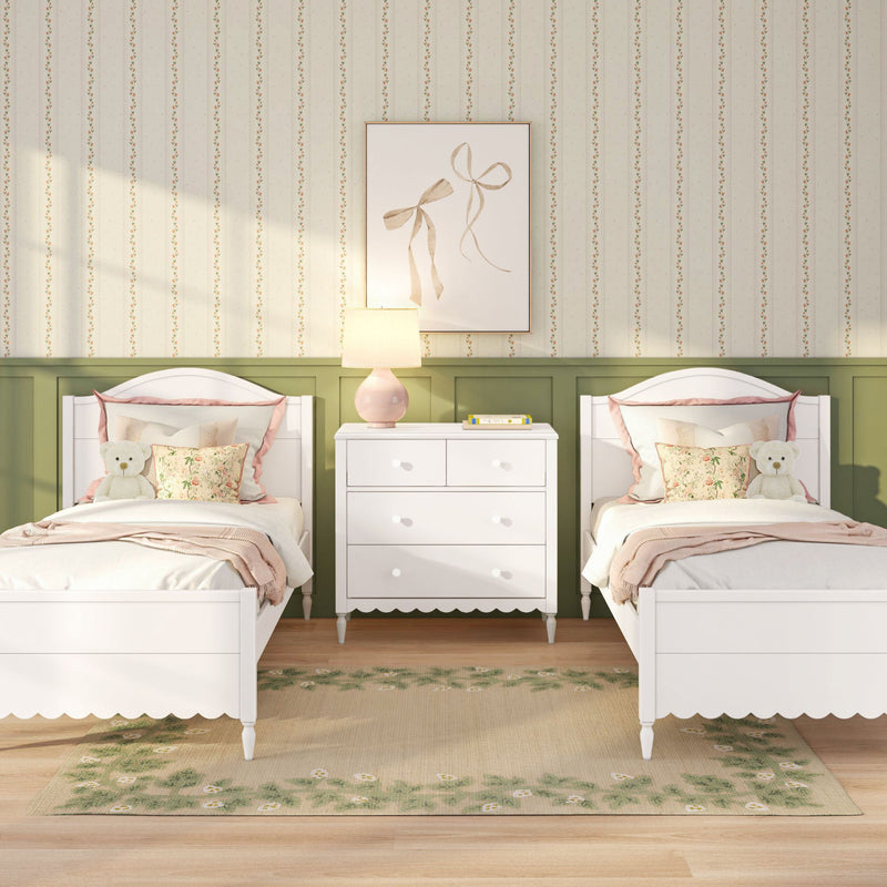 Twin white beds in a pastel pink and green children's bedroom with floral pillows, teddy bears, wallpaper and bedside lamp