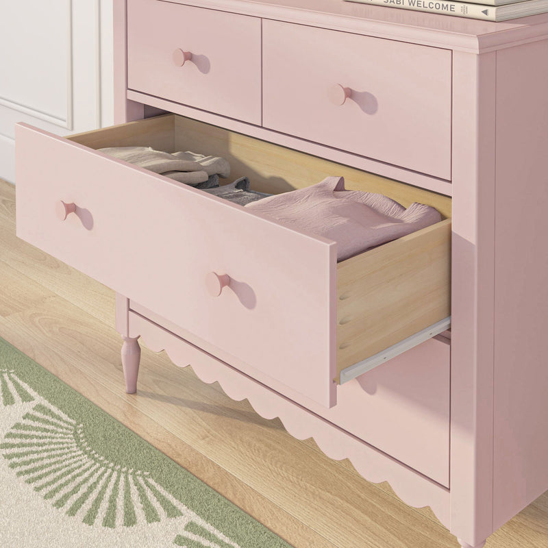Pastel pink wooden dresser with open drawer revealing folded children's clothes and linens, nursery storage furniture for baby room
