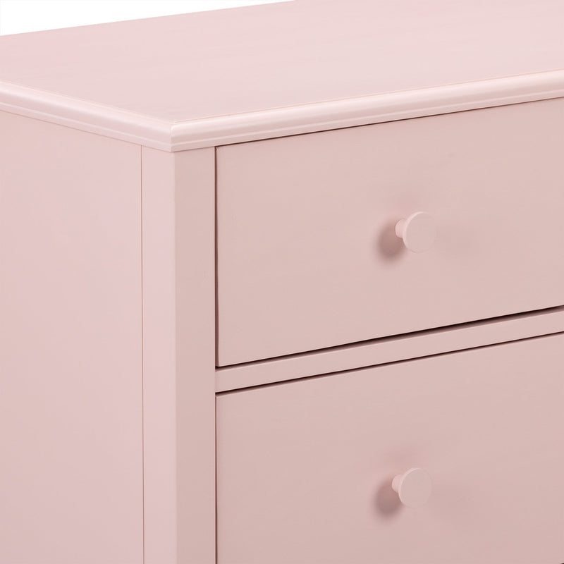 Close-up of blush pink wooden dresser top and drawers with round knob, modern nursery storage cabinet
