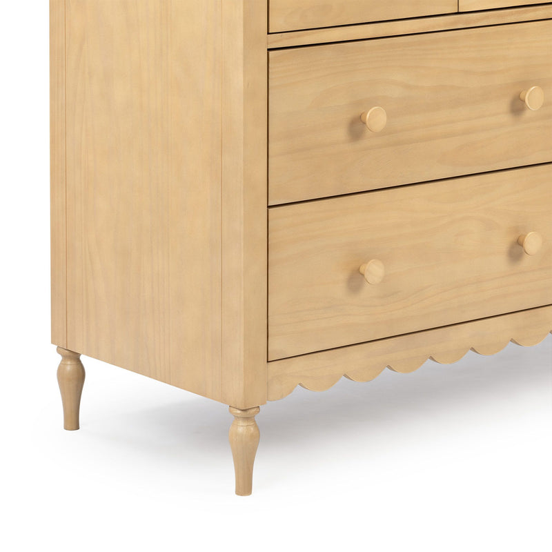 Close-up of light natural wood dresser (chest of drawers) with round wooden knobs, turned legs and scalloped apron — bedroom storage furniture