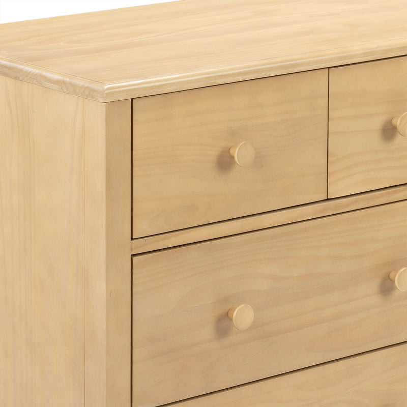 Close-up of light pine wood dresser with natural finish and round wooden knobs on a bedroom chest of drawers