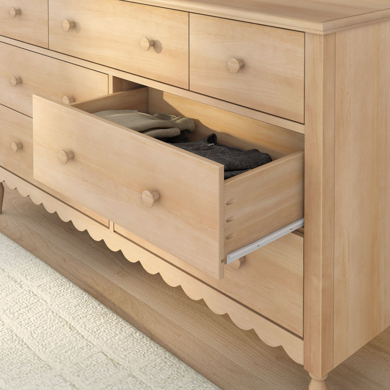 Light natural wood bedroom dresser with open drawer showing folded clothes, round wooden knobs and scalloped base