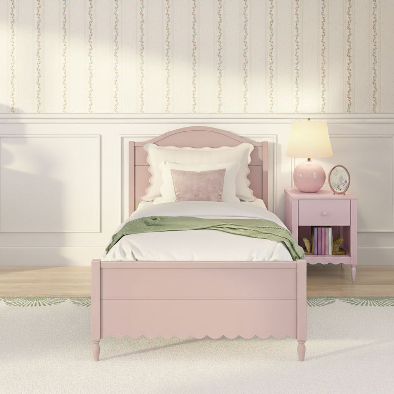Pastel pink twin bed with scalloped headboard, plush pillows and green throw, pink nightstand with lamp, floral striped wallpaper and white wainscoting