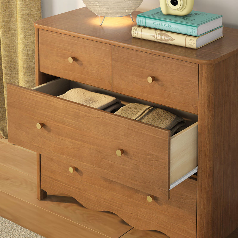 Mid-century modern walnut dresser chest of drawers with open drawers and brass knobs, folded linens inside and bedside lamp with stacked books on top, bedroom storage furniture
