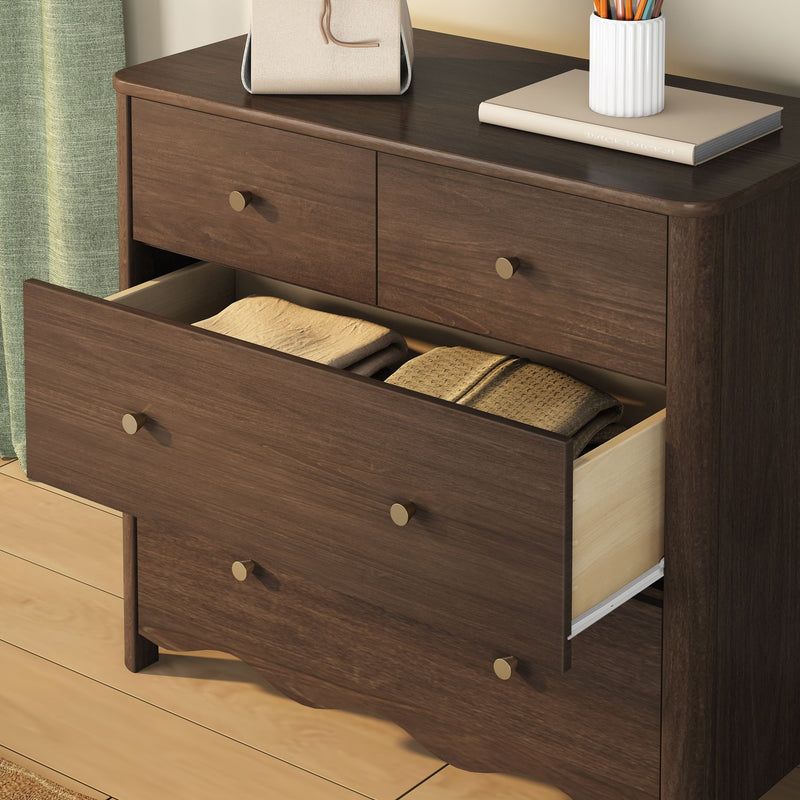 Dark walnut dresser with open drawers and folded blankets, brass round knobs, decorative book and pencil holder on top in a bedroom