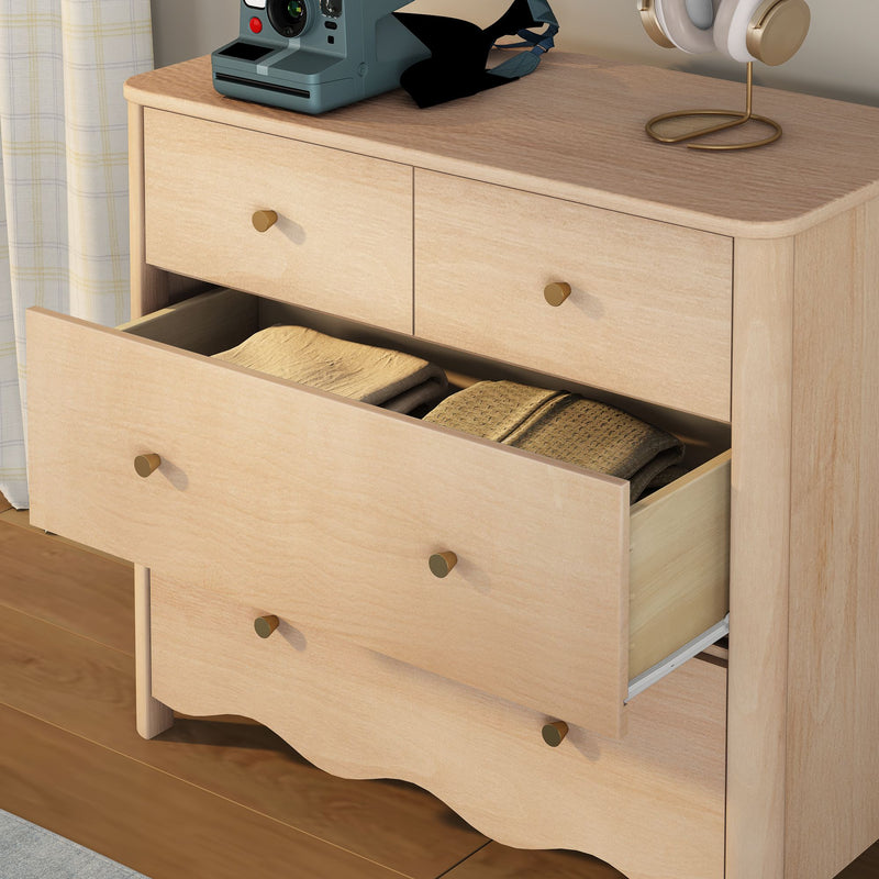 Light wood bedroom dresser with open drawer revealing folded blankets, brass knobs, instant camera and gold‑trim headphones on top — minimalist modern bedroom storage and decor