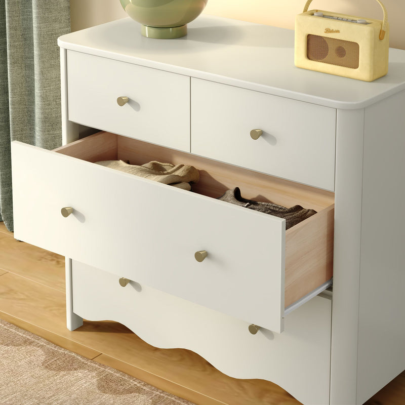 White wooden dresser bedroom storage with open drawer showing folded clothes, brass knobs and vintage radio and lamp on top by a hardwood floor
