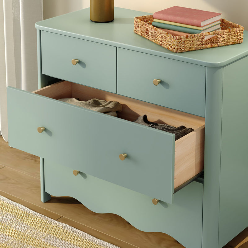 Mint green wooden dresser with brass knobs and open drawers revealing folded clothes, woven rattan tray with stacked books on top