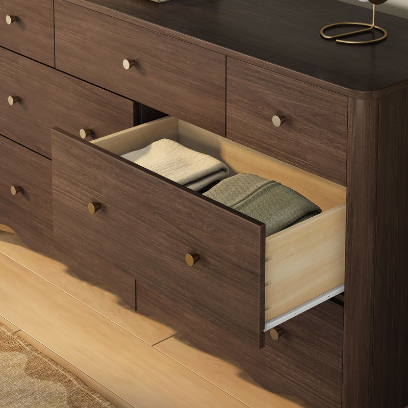 Walnut dresser with open drawer and folded clothes, brass knobs and dark wood top — modern bedroom storage on hardwood floor
