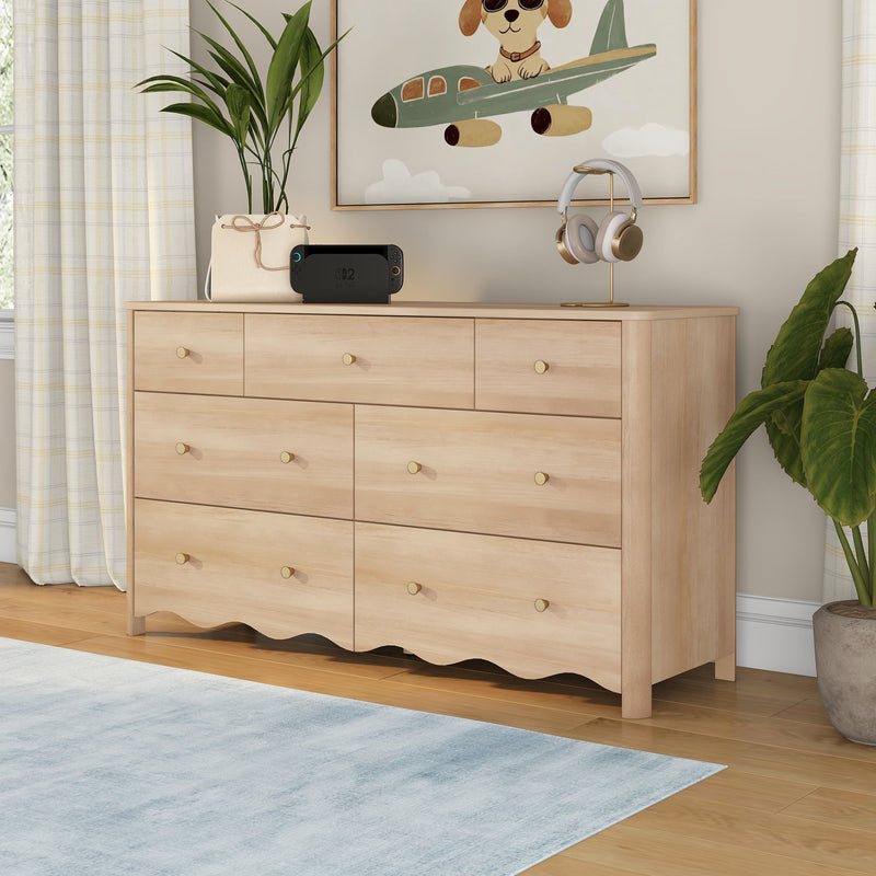 Light wood six-drawer dresser with brass knobs in a neutral nursery, airplane dog wall art, potted plant, headphones on stand and portable gaming console