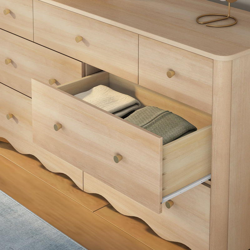Light wood bedroom dresser with brass knobs and an open drawer revealing neatly folded linens on hardwood floor — clothes storage chest