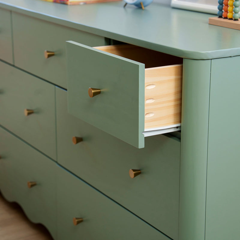 Sage green dresser with a partially open drawer exposing natural wood interior and brass cone knobs, modern bedroom storage cabinet
