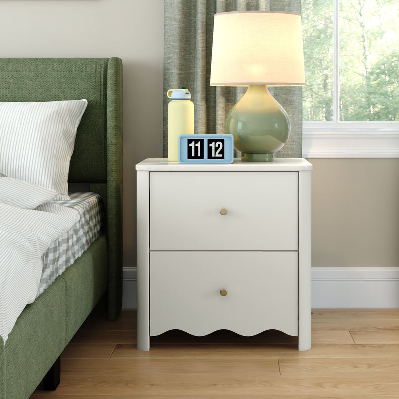 White nightstand with modern table lamp, blue flip alarm clock showing 11:12 and yellow water bottle beside a green upholstered bed in a bright modern bedroom with window view