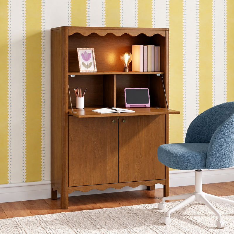 Wooden fold-down secretary desk in cozy home office nook with warm Edison lamp, stacked books, pink tablet, pencil cup and blue swivel chair against yellow striped wallpaper
