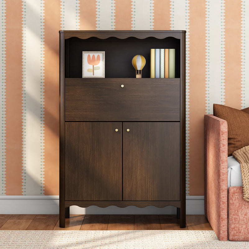 Dark wood storage cabinet with scalloped trim, framed flower art, toy hot air balloon and pastel books against peach striped nursery wallpaper