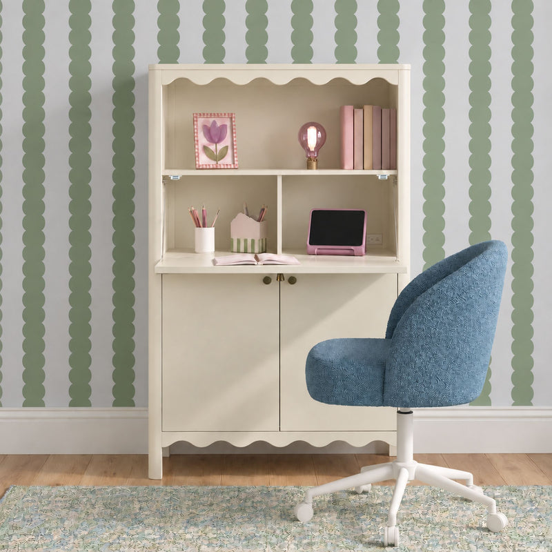 Kids desk with cream scalloped hutch, pink lamp and tablet, blue upholstered swivel chair, mint green scallop-stripe wallpaper and patterned rug