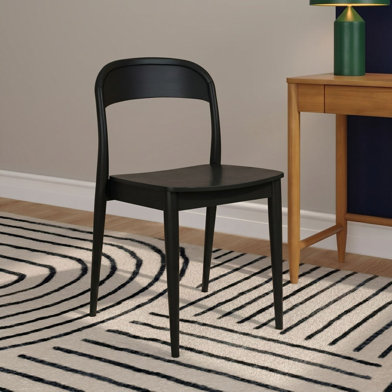 Modern black wooden dining chair next to a light oak side table with a green lamp on a black-and-white striped rug in a minimalist interior.